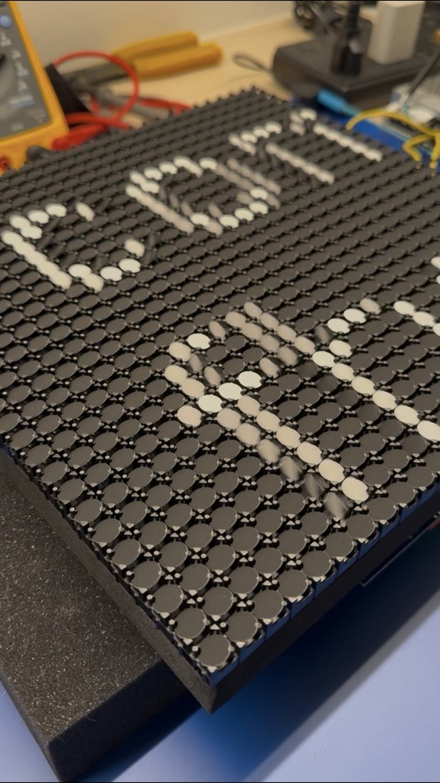 A flipdot panel angled on the workbench with
                     some dots flipped white to form characters