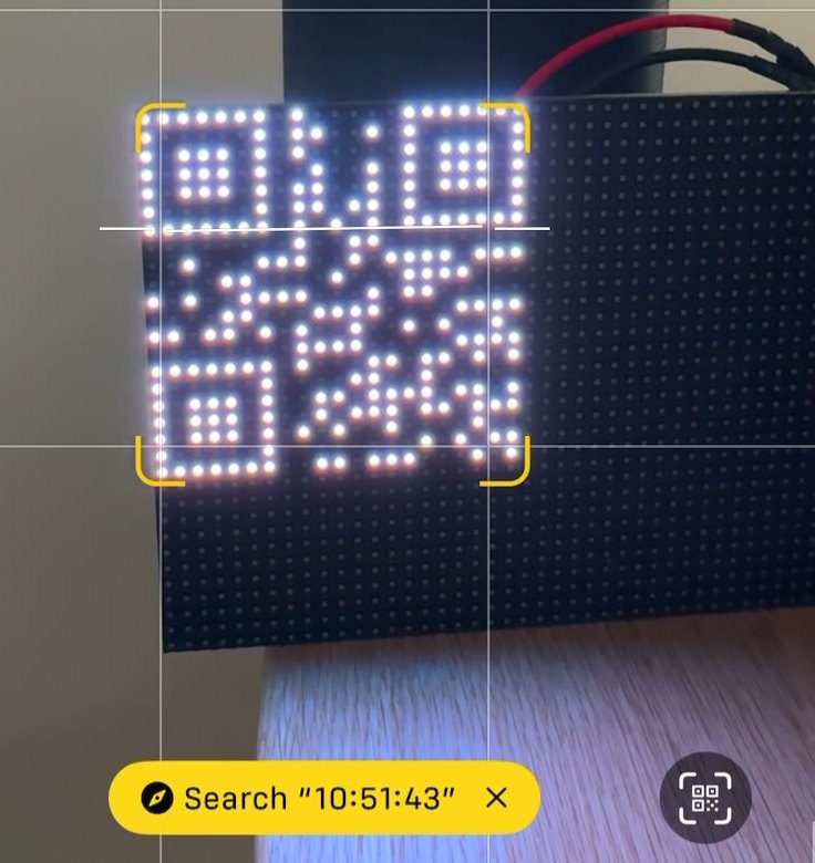 A phone camera pointed at an LED matrix
                     showing a QR code, with the phone having decoded it and offering to
                     search for the time it contains