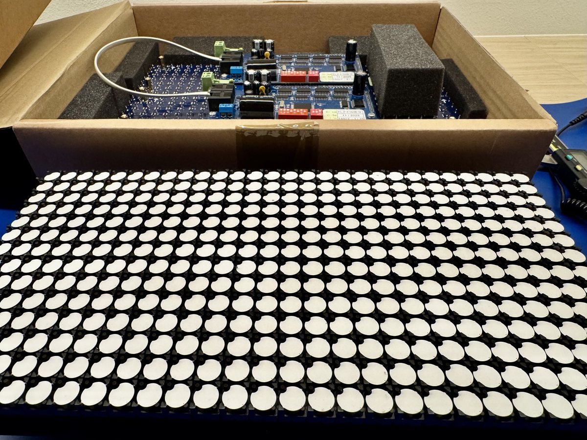 A flipdot panel with every dot flipped to
                     white, and behind it a second panel in its box, driver board upward